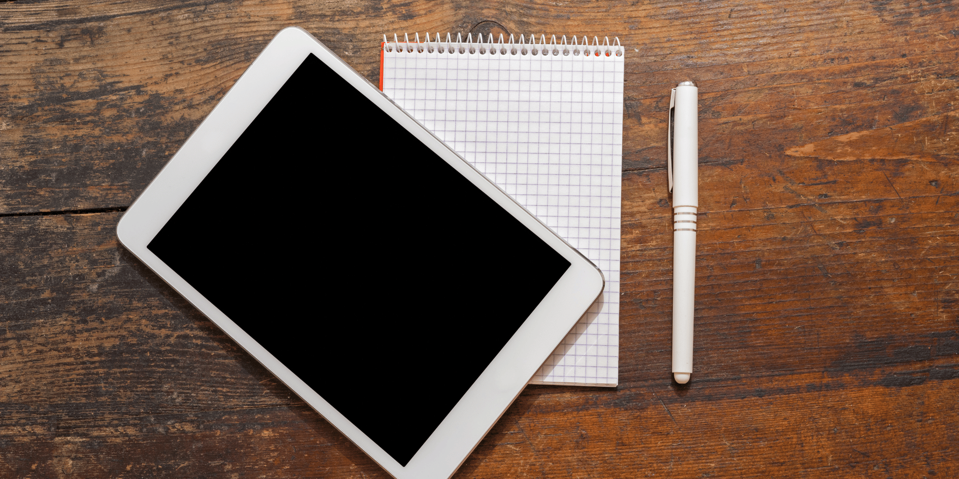 Tablet with black screen placed on a notepad and pen on a wooden desk – representing device diagnostics and tune-up concept.